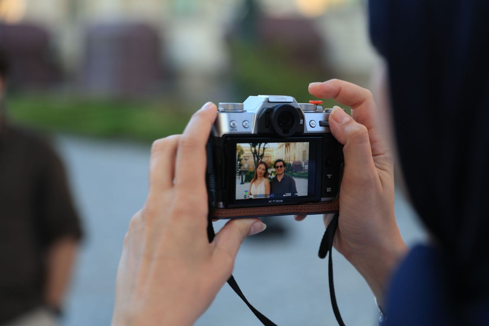 Hände halten eine Kamera und fotografieren ein Paar im Freien